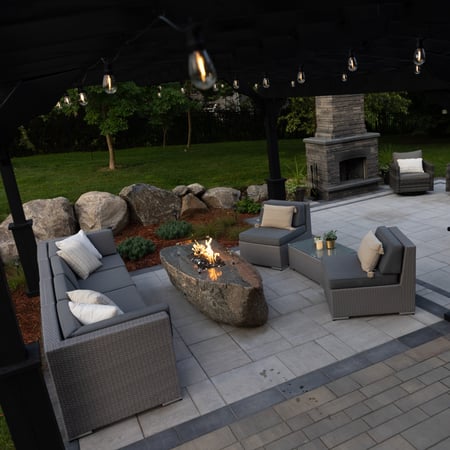 a covered patio with stone fire feature and comfy chairs