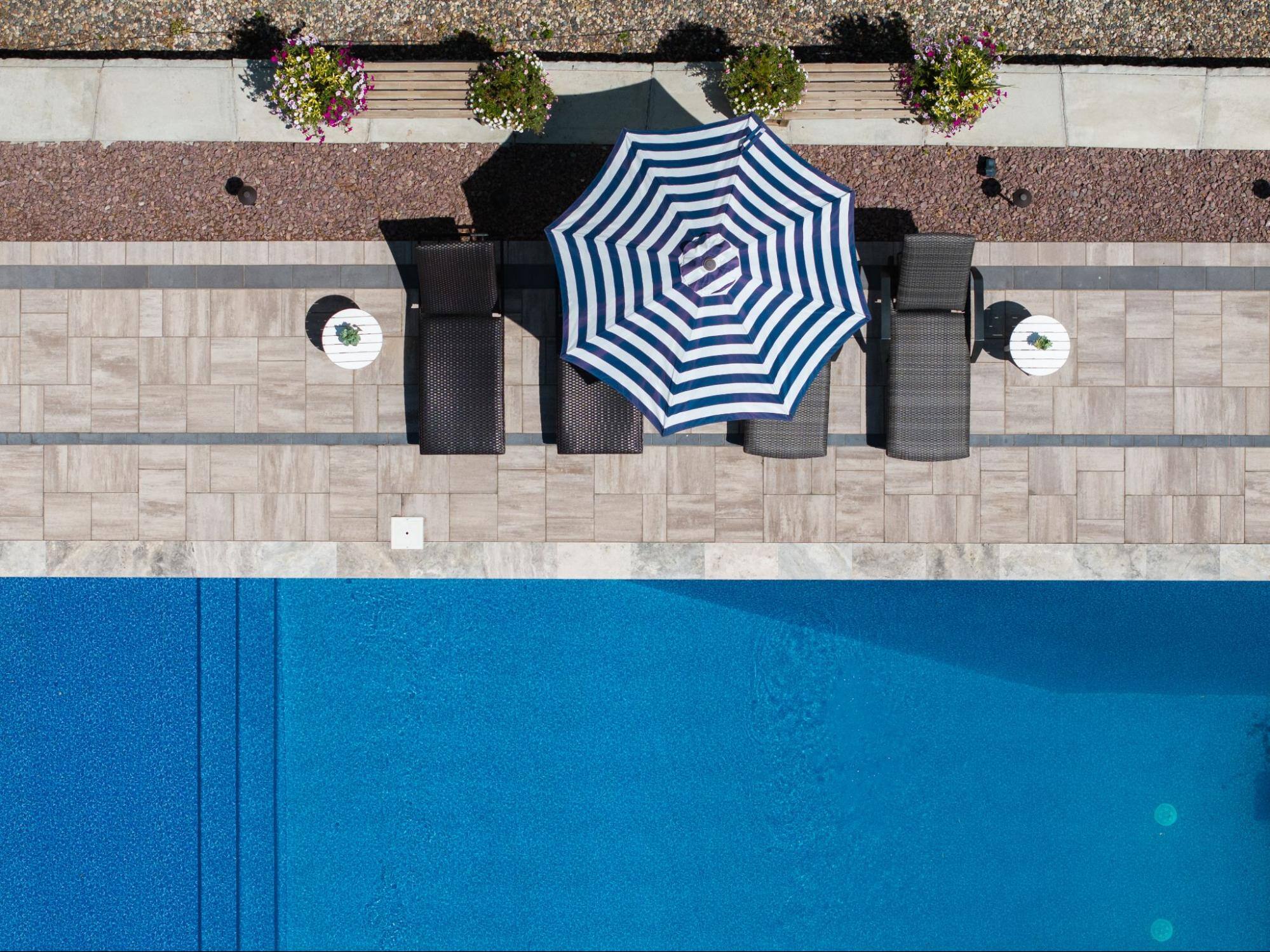 aerial shot of an in-ground pool. next to the pool are chairs covered by an umbrella.