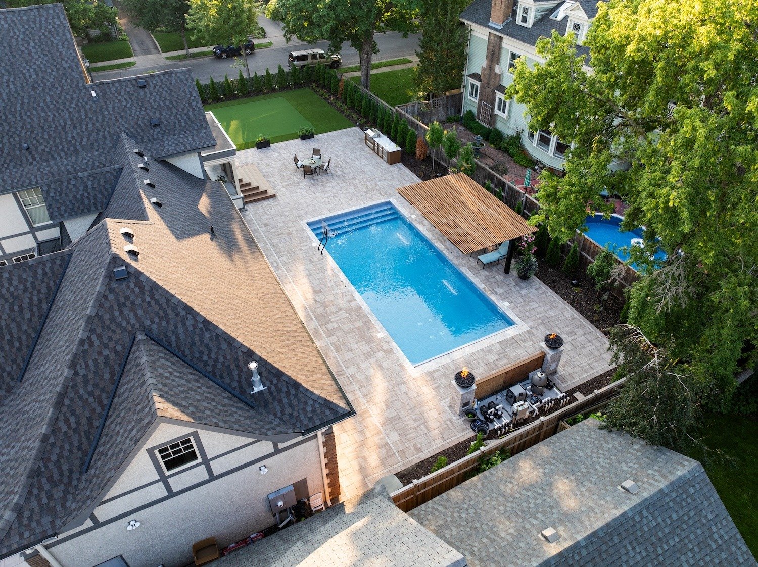 aerial shot of a backyard with a swimming pool, outdoor kitchen, and large hardscaped paver.