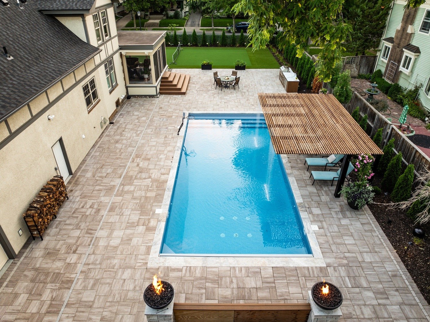 aerial shot of a backyard with a swimming pool, outdoor kitchen, and large hardscaped paver.