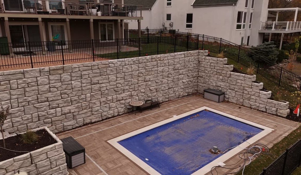 the after shot of a completed pool project. a large pool is surrounded by high-quality pavers and a beautiful stone retaining wall.