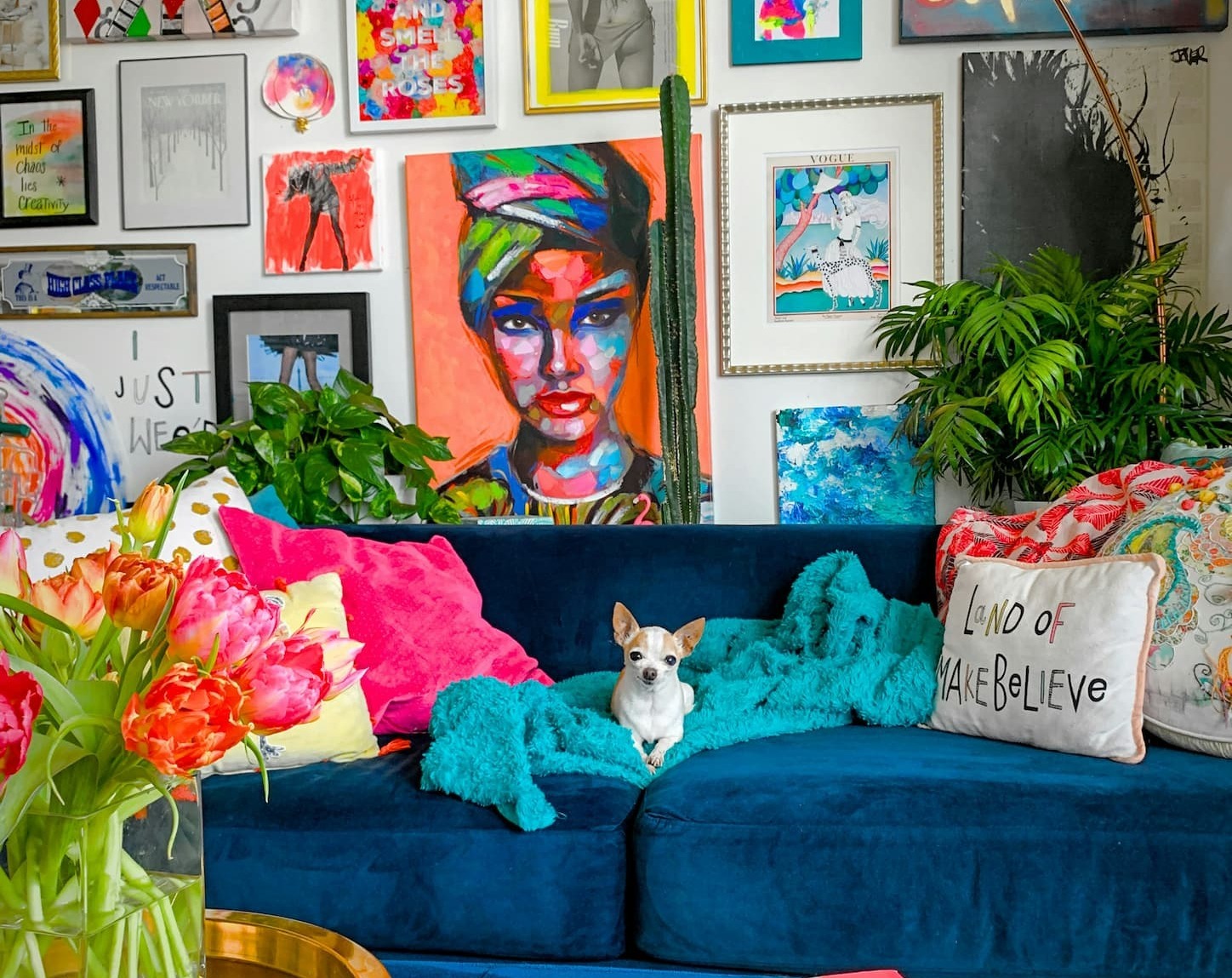 a colorful maximalist living room. a bright blue couch with colorful pillows with a lounging dog. Behind is an eclectic gallery wall.