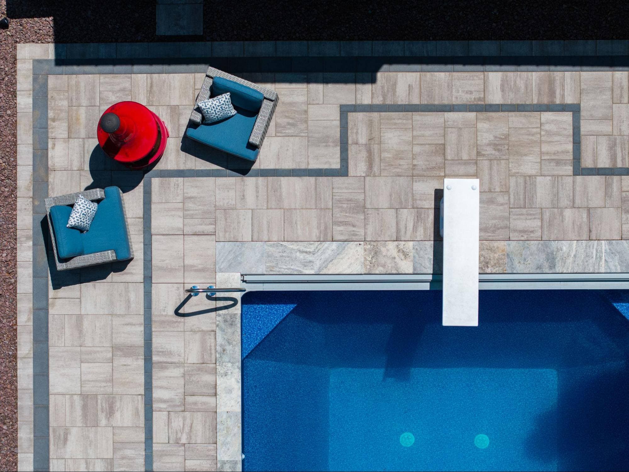 an aerial shot of an in-ground pool. nearby are several bright blue chairs and a vivid red table.