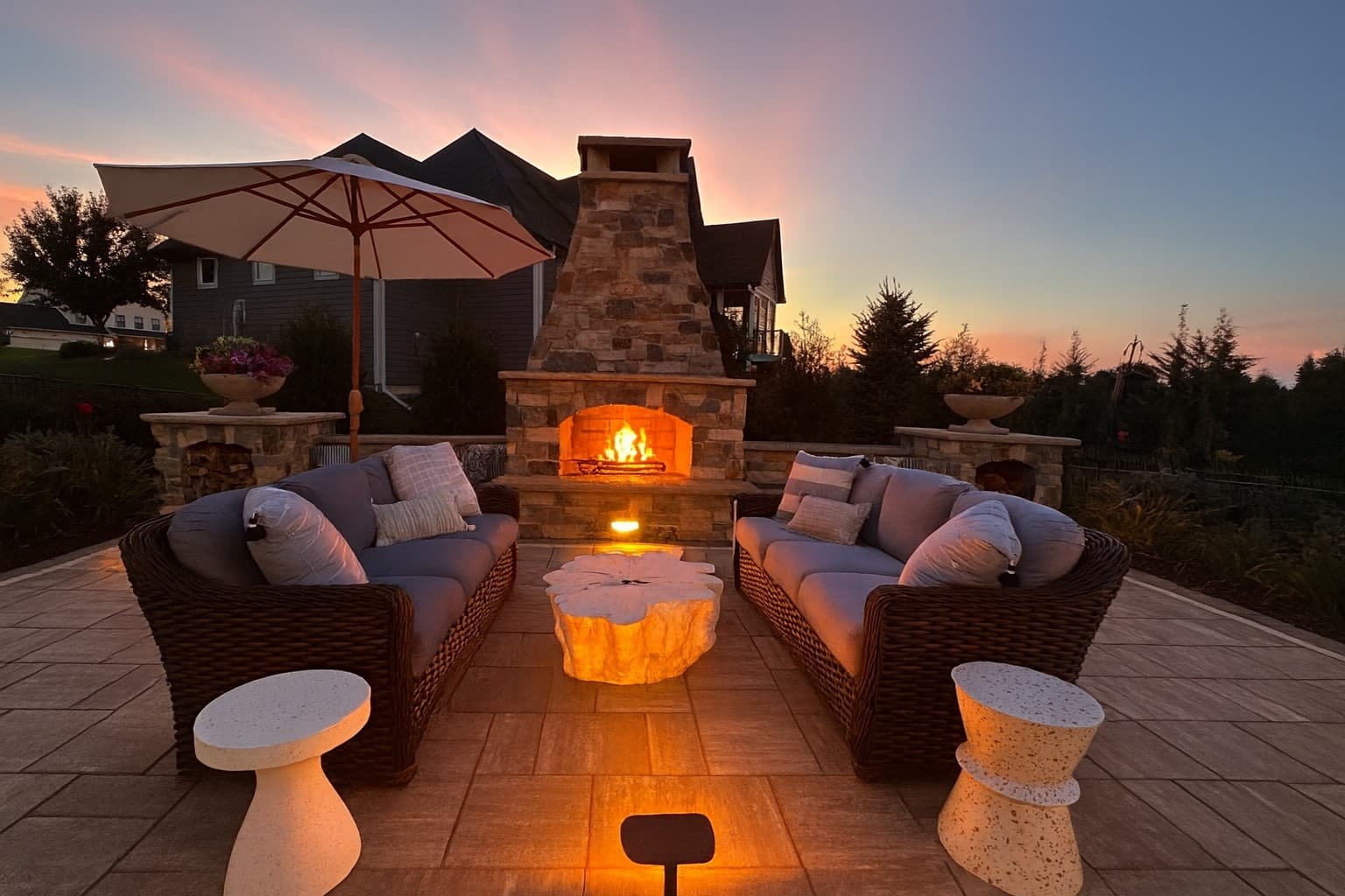 an outdoor fireplace with gorgeous brick pattern. in front of the fireplace is a seating area with couches, end tables, and a sun umbrella.