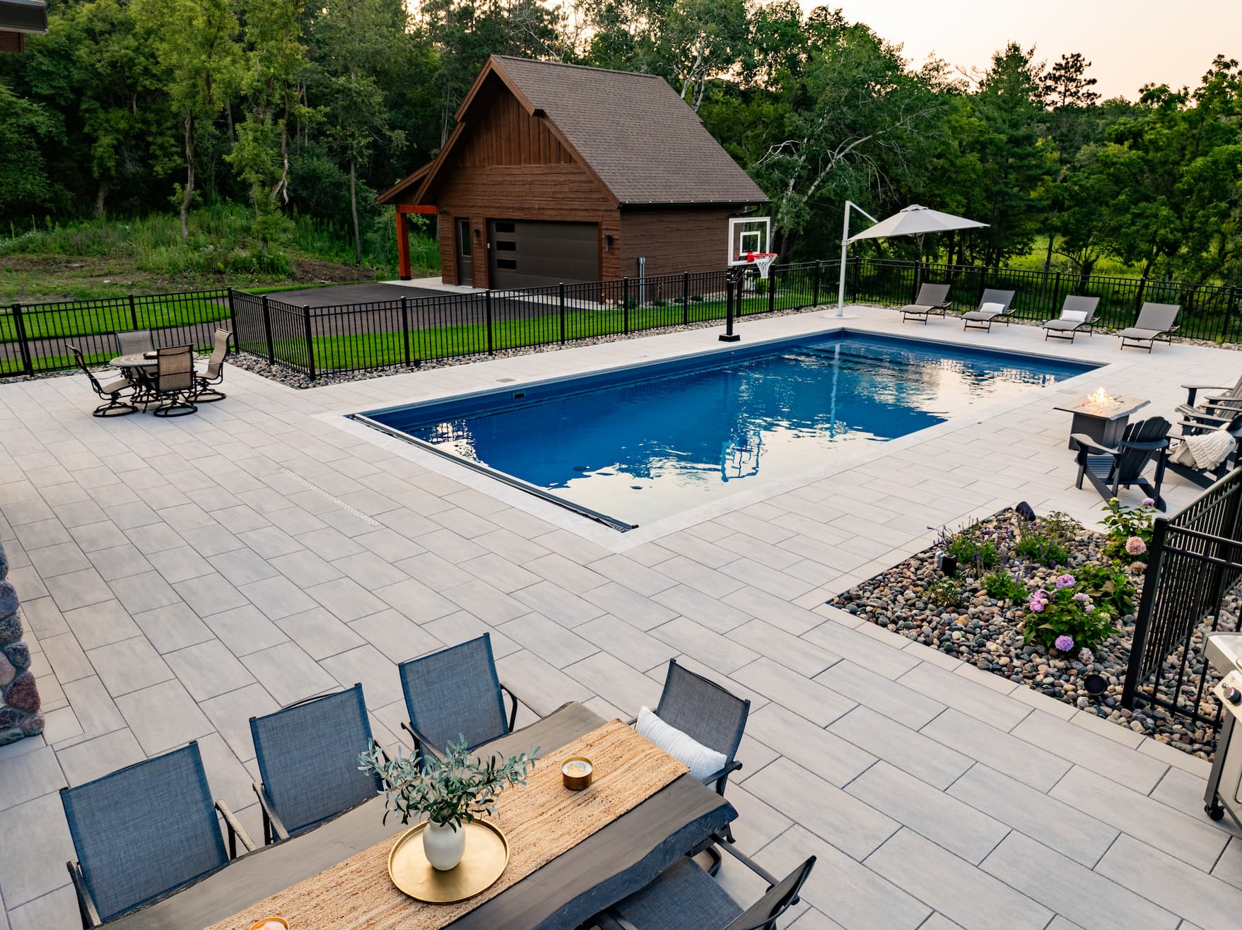 a backyard with beautiful hardscaped pavers, a large dining table, and an in-ground pool with basketball hoop.