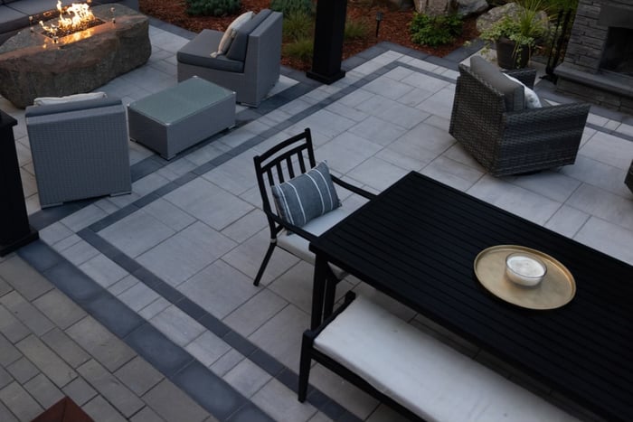 a candle ontop of a table in an outdoor living room. in the distance is a fire table with surrounding lounge chairs.