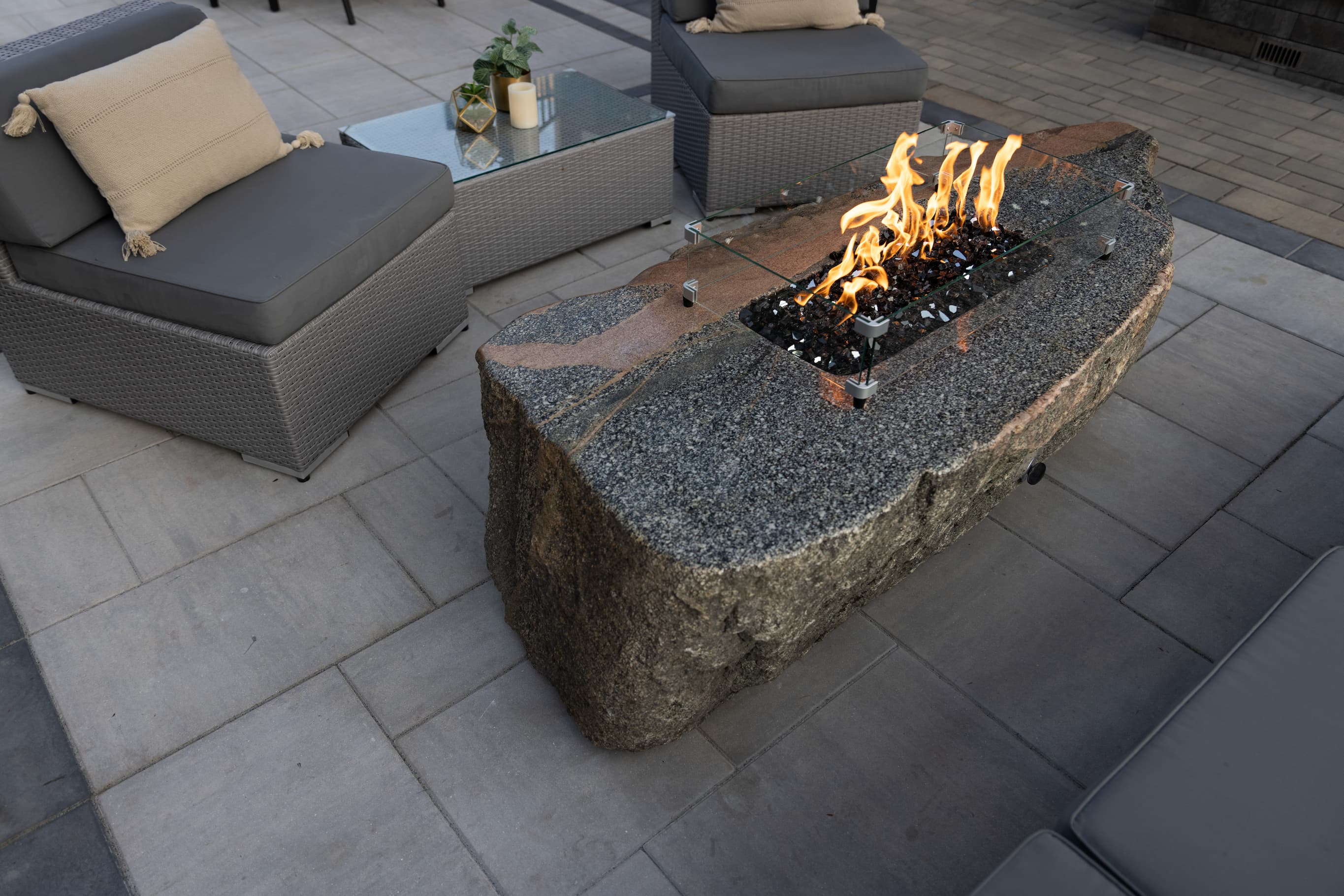 a gas-controlled fire table next to lounging chairs in a backyard