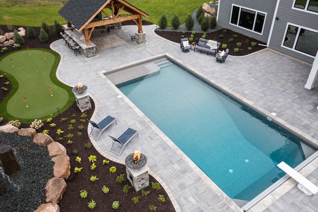 an in-ground pool with a tanning ledge, stairs, and a diving board