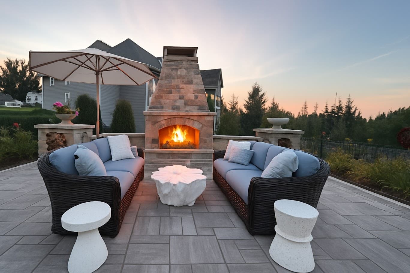 an outdoor living room with a bespoke stone fireplace. nearby are comfy blue couches with wicker siding and a stunning set of two matching marble end tables with a complementary marble coffee table.