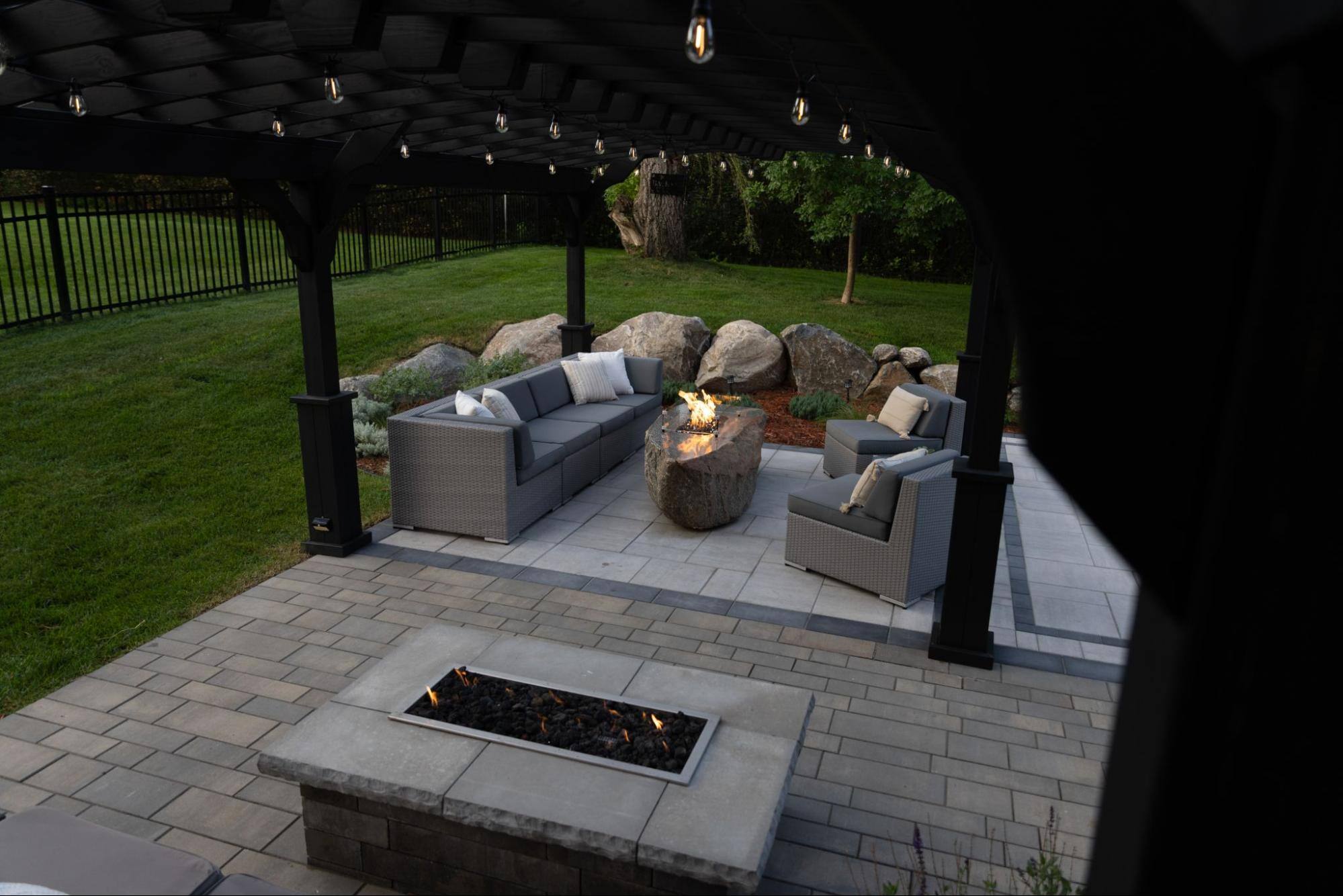 a pergola overlooking an outdoor living room with fire feature. the pergola is lined with small lights in the roof.