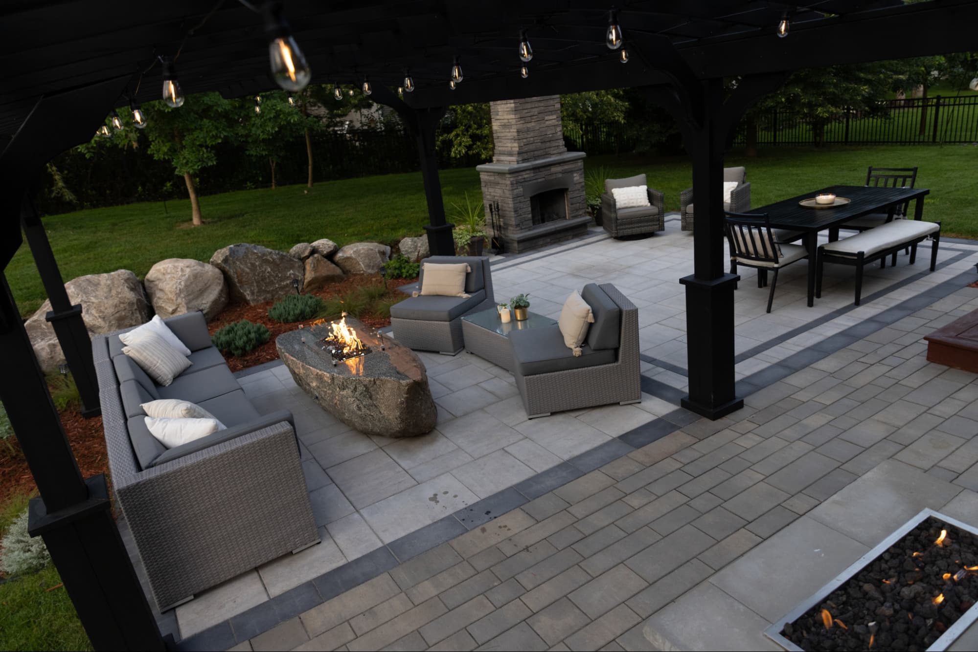 a black pergola over an outdoor living room with gray furniture and gray hardscaping.