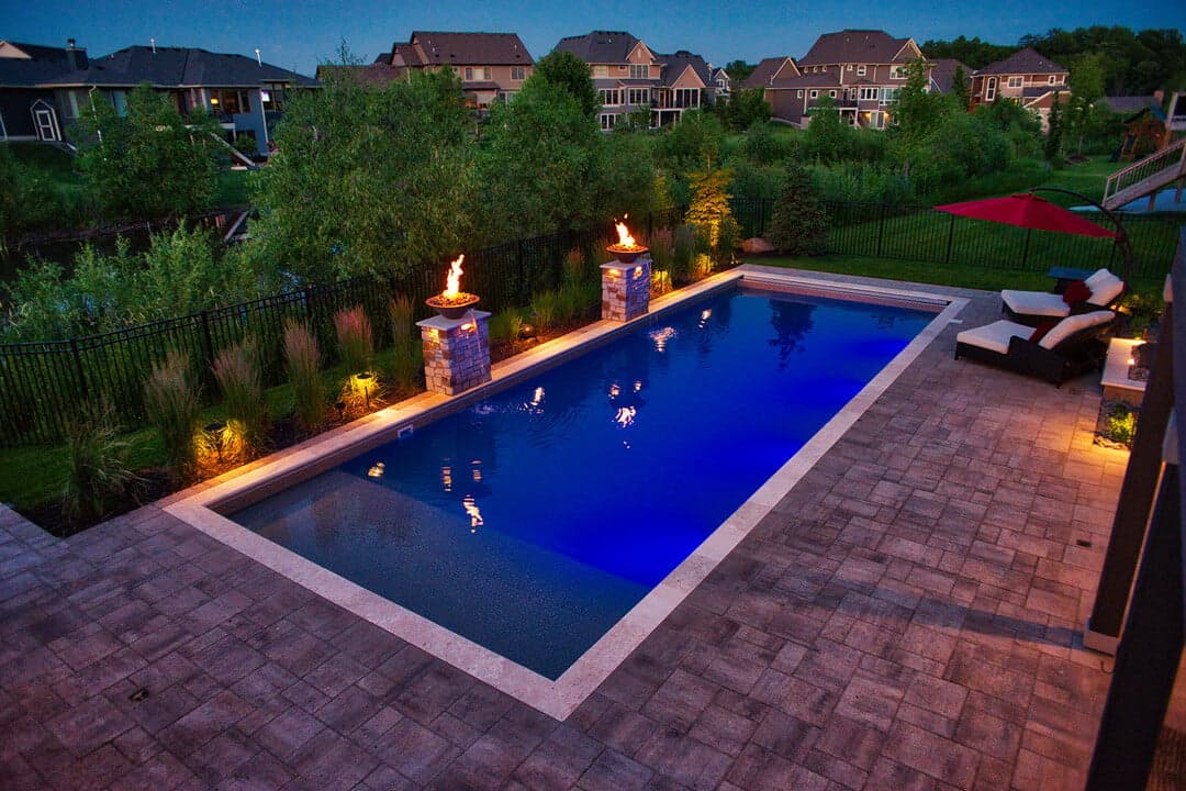 a pool at nighttime with surrounding fire features (fire bowls) providing light