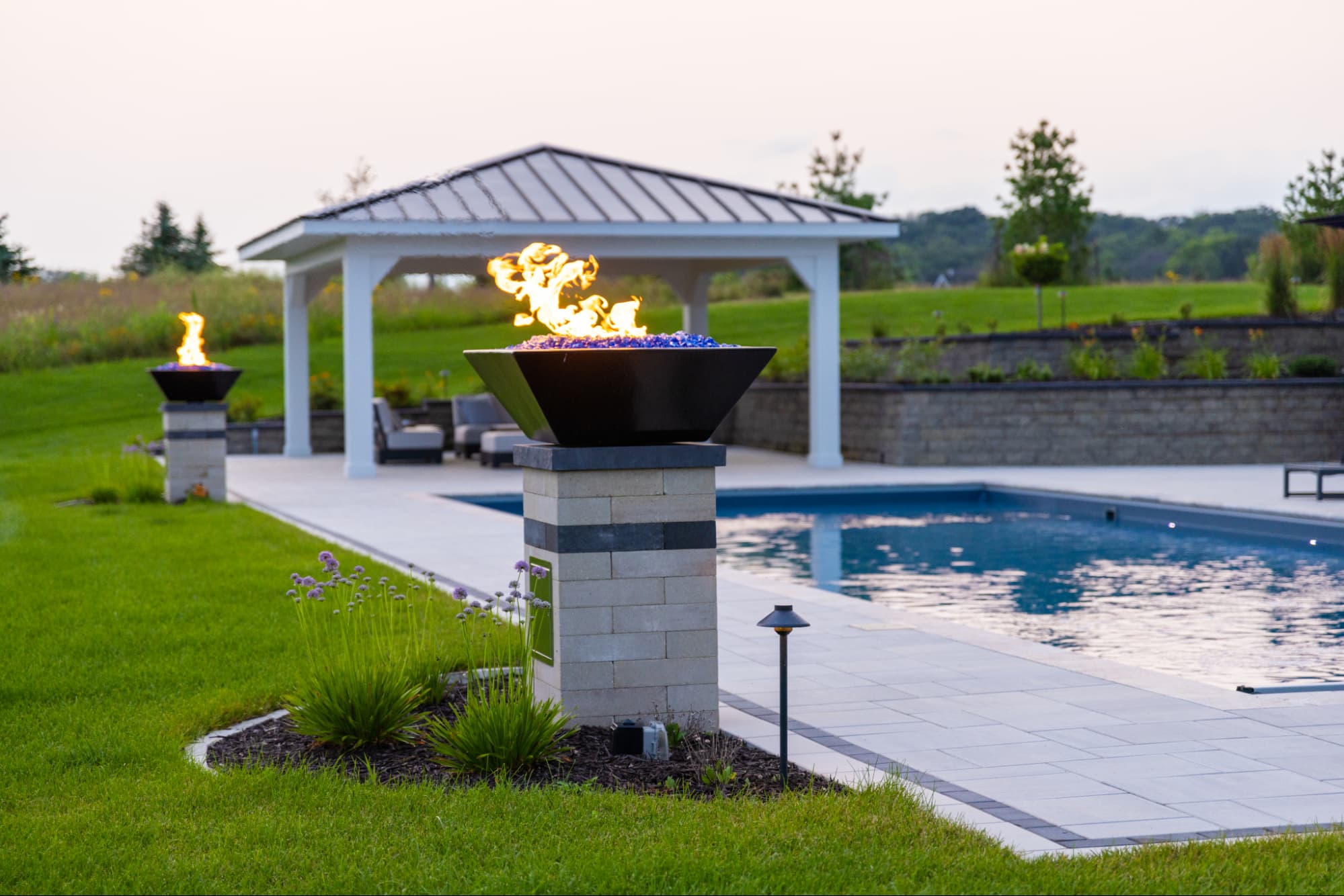 a fire bowl ontop of a pedestal, next to an in-ground swimming pool