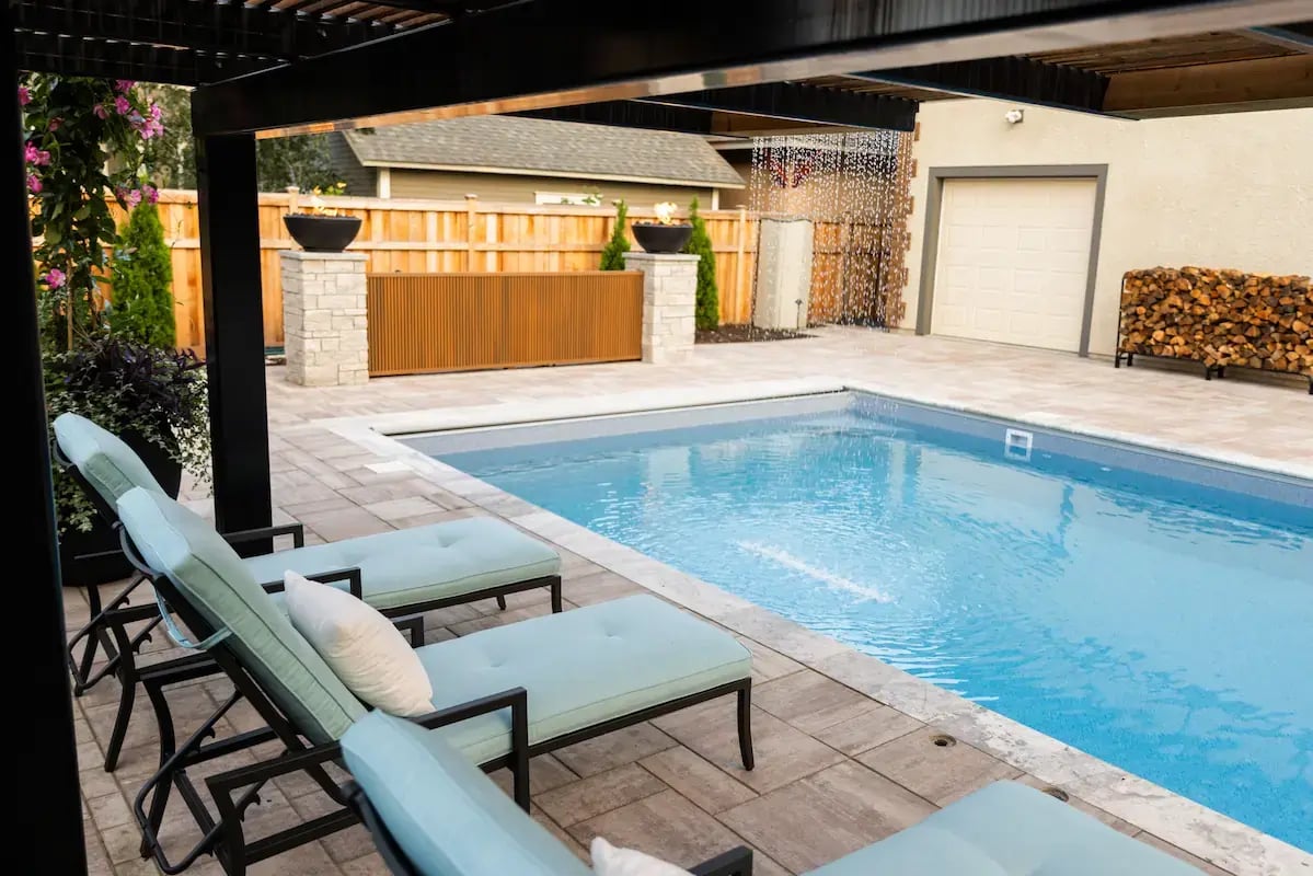 Side view of a blue pool with paver pool deck and blue chairs