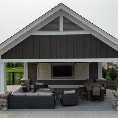 a gray building with an outdoor couch and a tv mounted under the overhang
