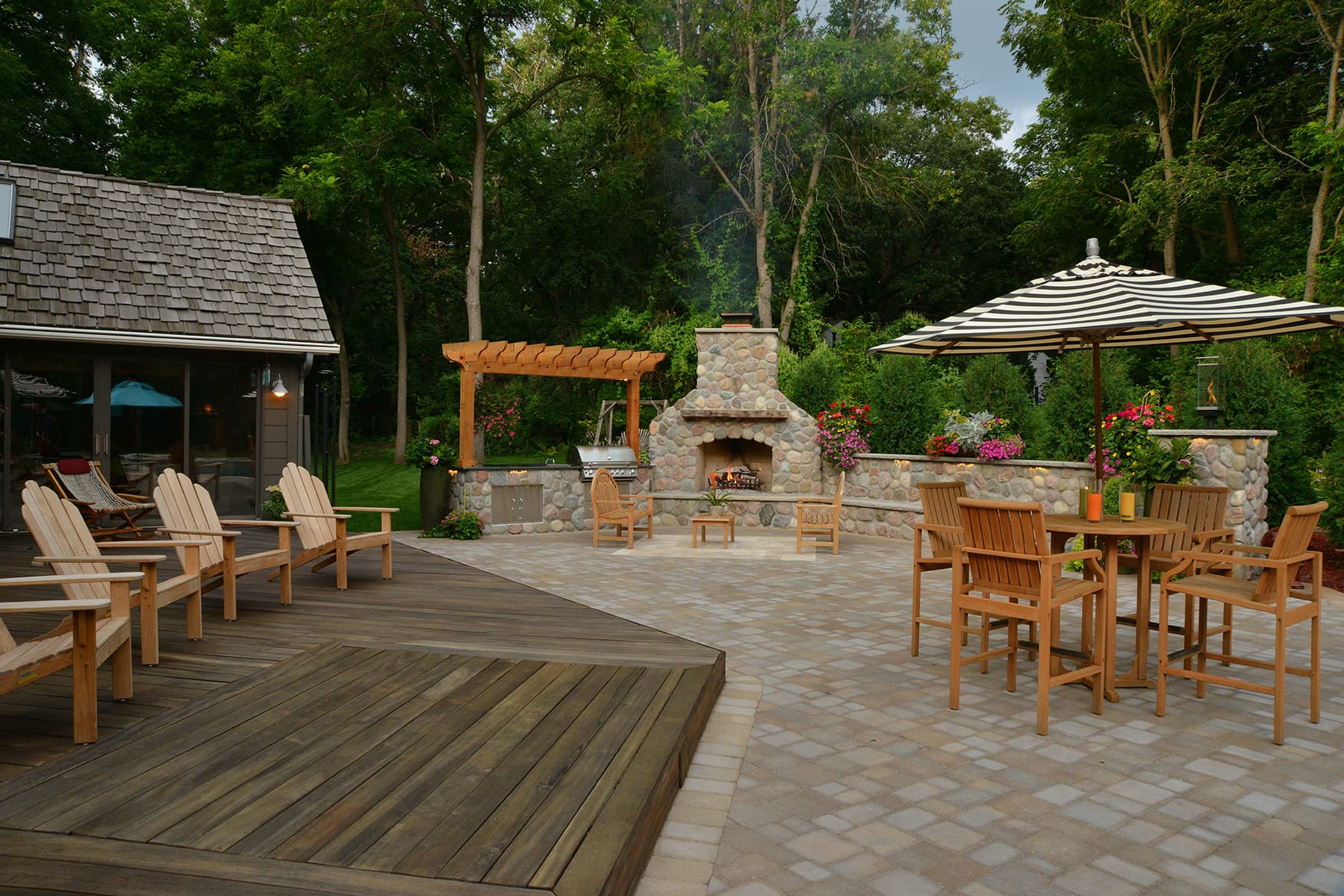 an outdoor kitchen with a custom stone fireplace, wooden patio, and shaded dining areas.