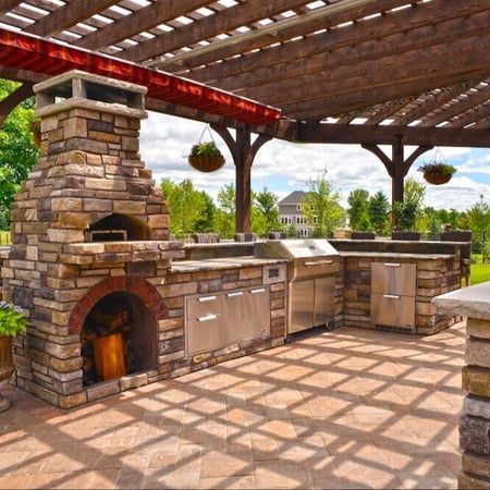 an outdoor kitchen with a pizza oven, traditional grill, and ample storage. the pizza oven and counters are made out of multicolored bricks.
