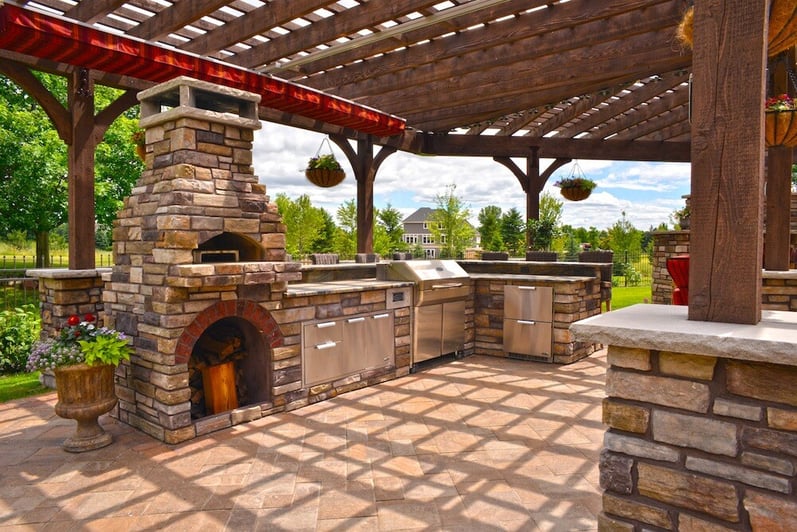 an outdoor kitchen with a pizza oven, traditional grill, and ample storage. the pizza oven and counters are made out of multicolored bricks.