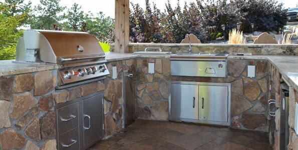 Outdoor kitchen area with stone countertops and stainless steel grill and sink