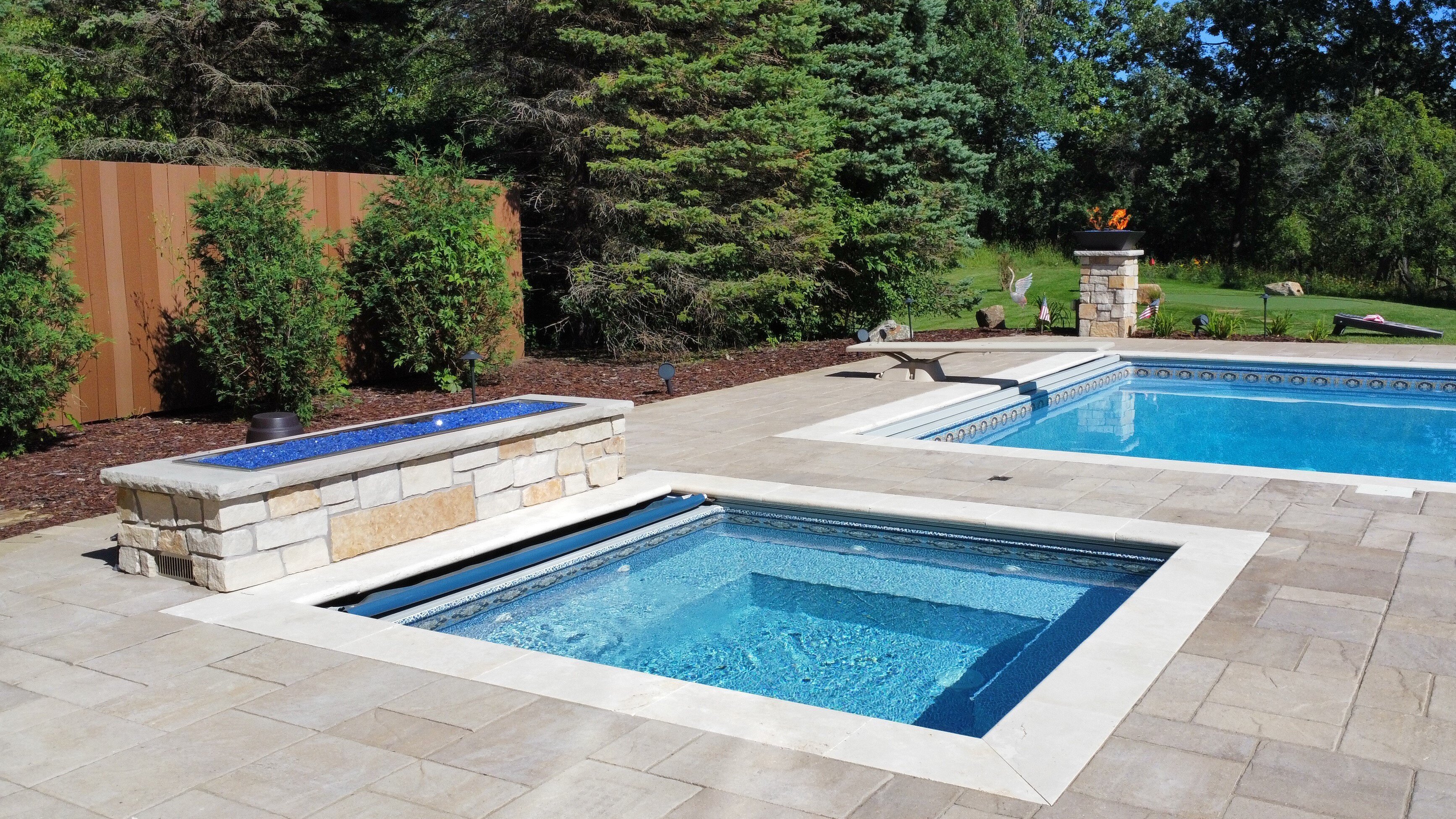 an outdoor pool with nearby outdoor hot tub. Both are surrounded by neutral gray pavers.