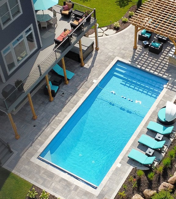 aerial view of a backyard pool surrounded by paver patio pool deck and blue lounge chairs