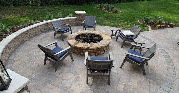 patio chairs surrounding a stone firepit on a circular paver patio.