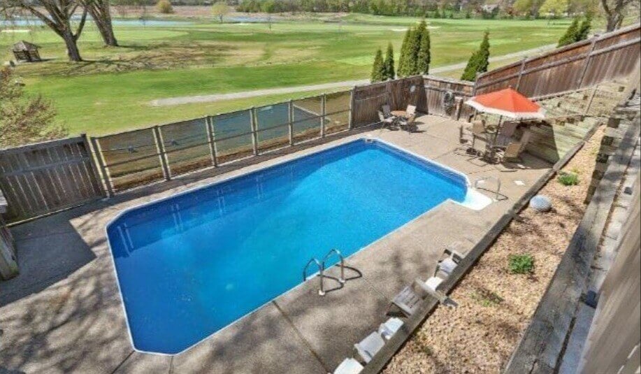 a before shot of a backyard pool. it's a decent size, but is cramped and the surrounding fence is weather-damaged.