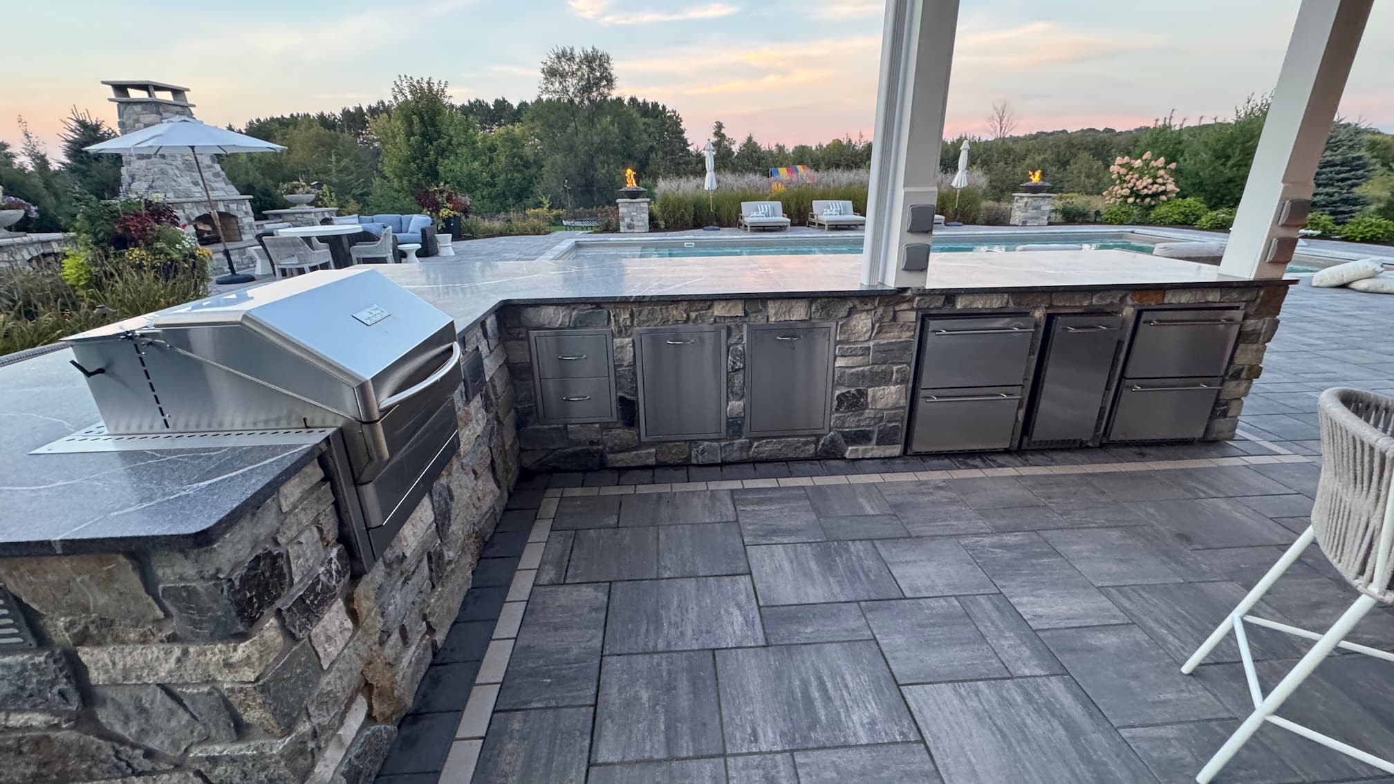 an outdoor kitchen with gorgeous stone cabinets and top of the line built-in appliances: grill, mini fridge, mini freezer, dishwasher, ice cabinet, and more.